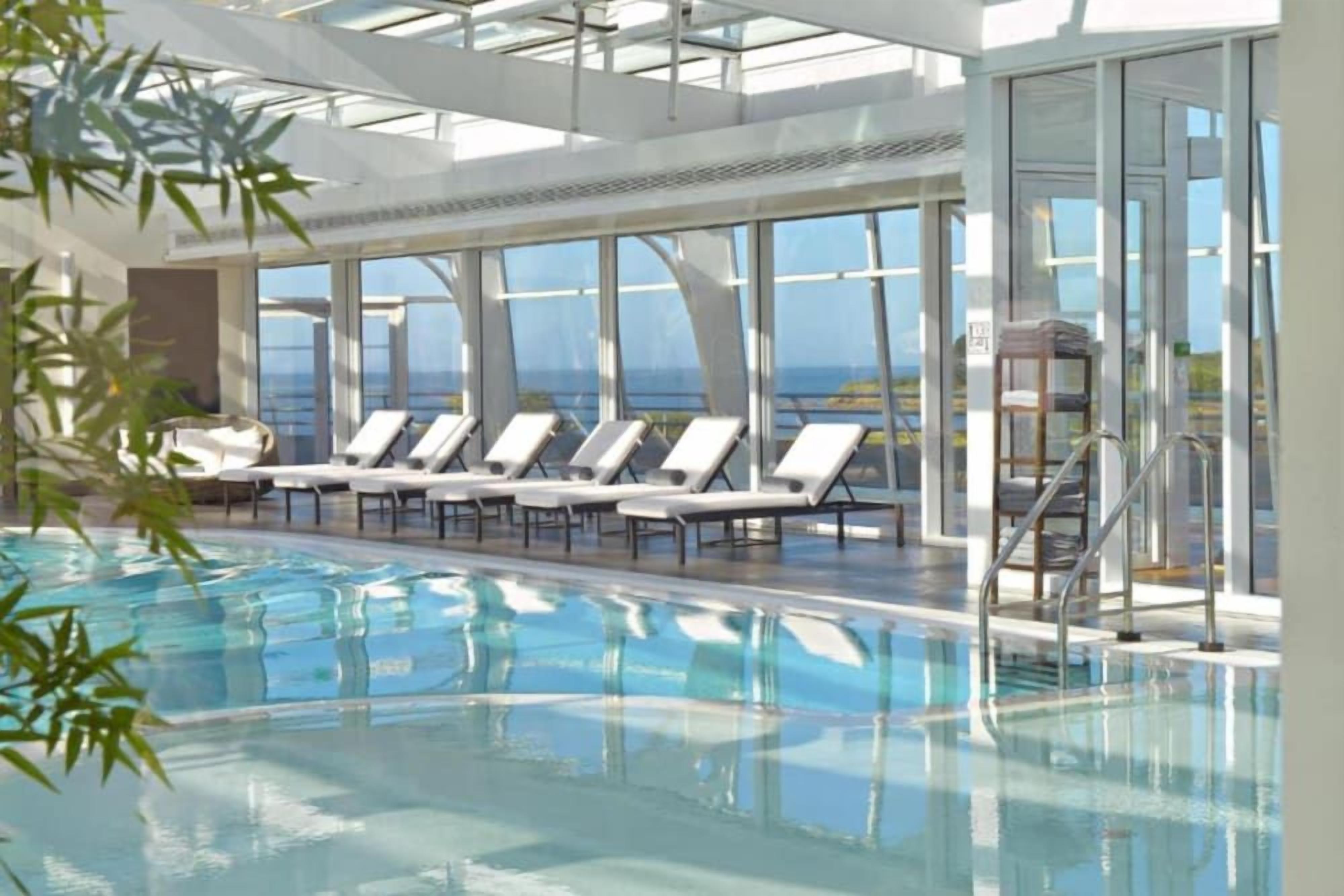 Un espace piscine avec des chaises longues et une structure fermée par des parois de verre.