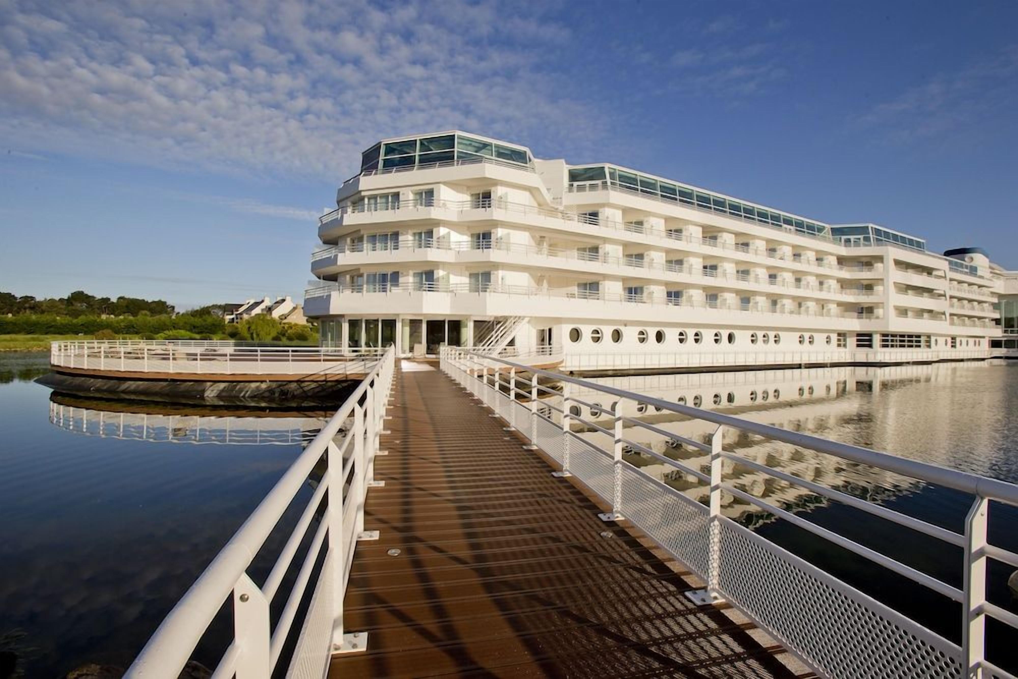 Un hôtel à plusieurs étages offrant une vue sur le front de mer, doté d’une promenade couverte et d’un quai pour bateaux.
