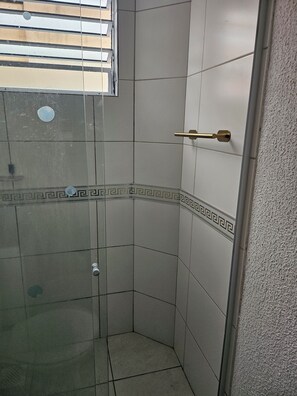 A corner shower with a door, tiled walls, and a window with blinds.