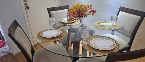A dining table with four chairs, a vase with flowers, and a glass on the table.