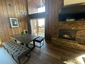A dining area with a wooden table and benches, a fireplace, and a view through a glass door. - Sierra Sky Retreat, Sleeps 6, Mountain Views, Pool/Hot Tubs, Near Canyon Lodge (Mammoth Lakes)