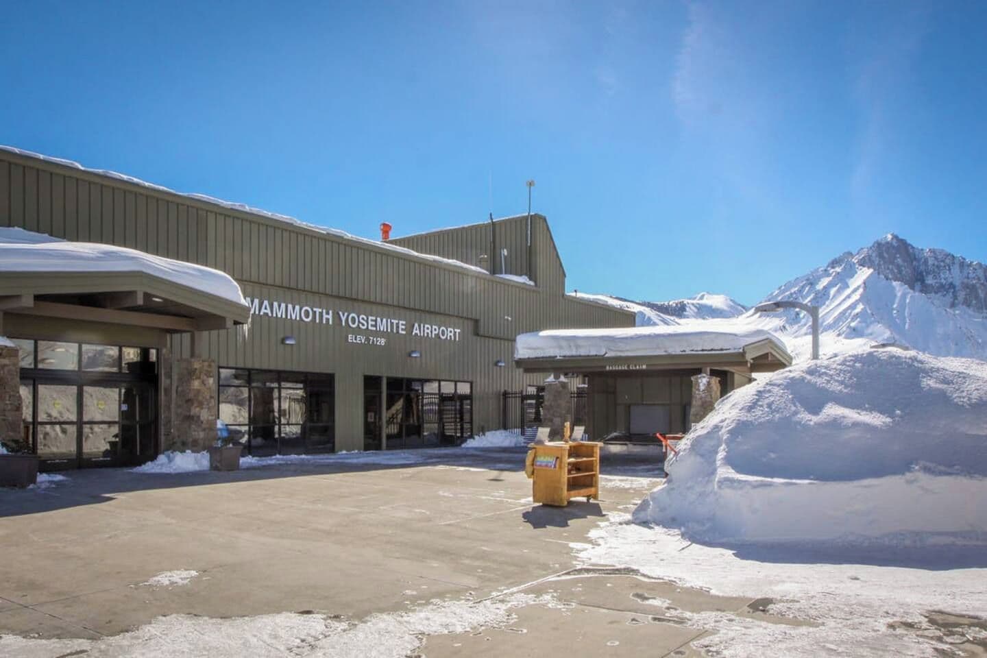 Exterior do Aeroporto Mammoth Yosemite, com o solo coberto de neve e montanhas ao fundo.