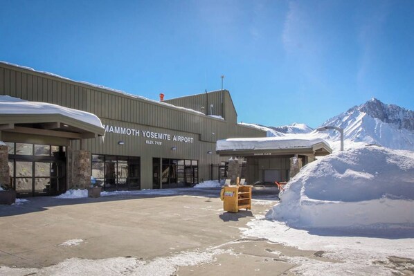 The exterior of Mammoth Yosemite Airport with snow-covered ground and mountains in the background. - Sierra Sky Retreat, Sleeps 6, Mountain Views, Pool/Hot Tubs, Near Canyon Lodge (Mammoth Lakes)