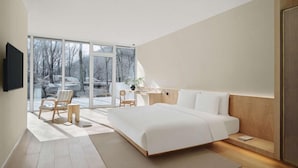 A modern bedroom with a large bed, a desk, and a chair, a flat-screen TV mounted on the wall, and a sliding glass door leading to a balcony. - Commune by the Great Wall Managed by Kempinski (Beijing)