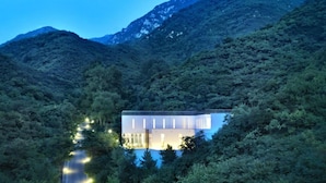 A modern building with a flat roof, surrounded by dense forest and mountains in the background. - Commune by the Great Wall Managed by Kempinski (Beijing)