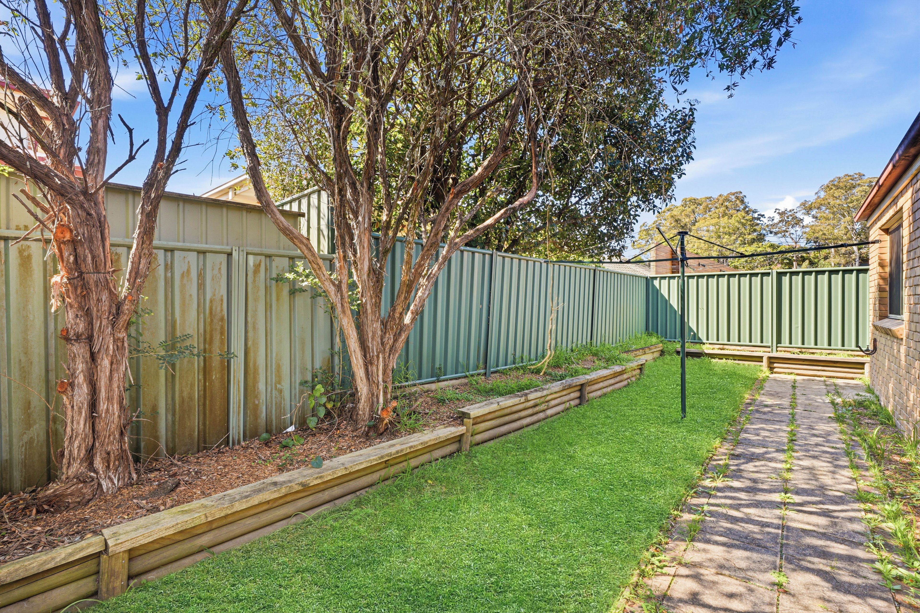 A backyard with a wooden deck, a green fence, and a paved path.