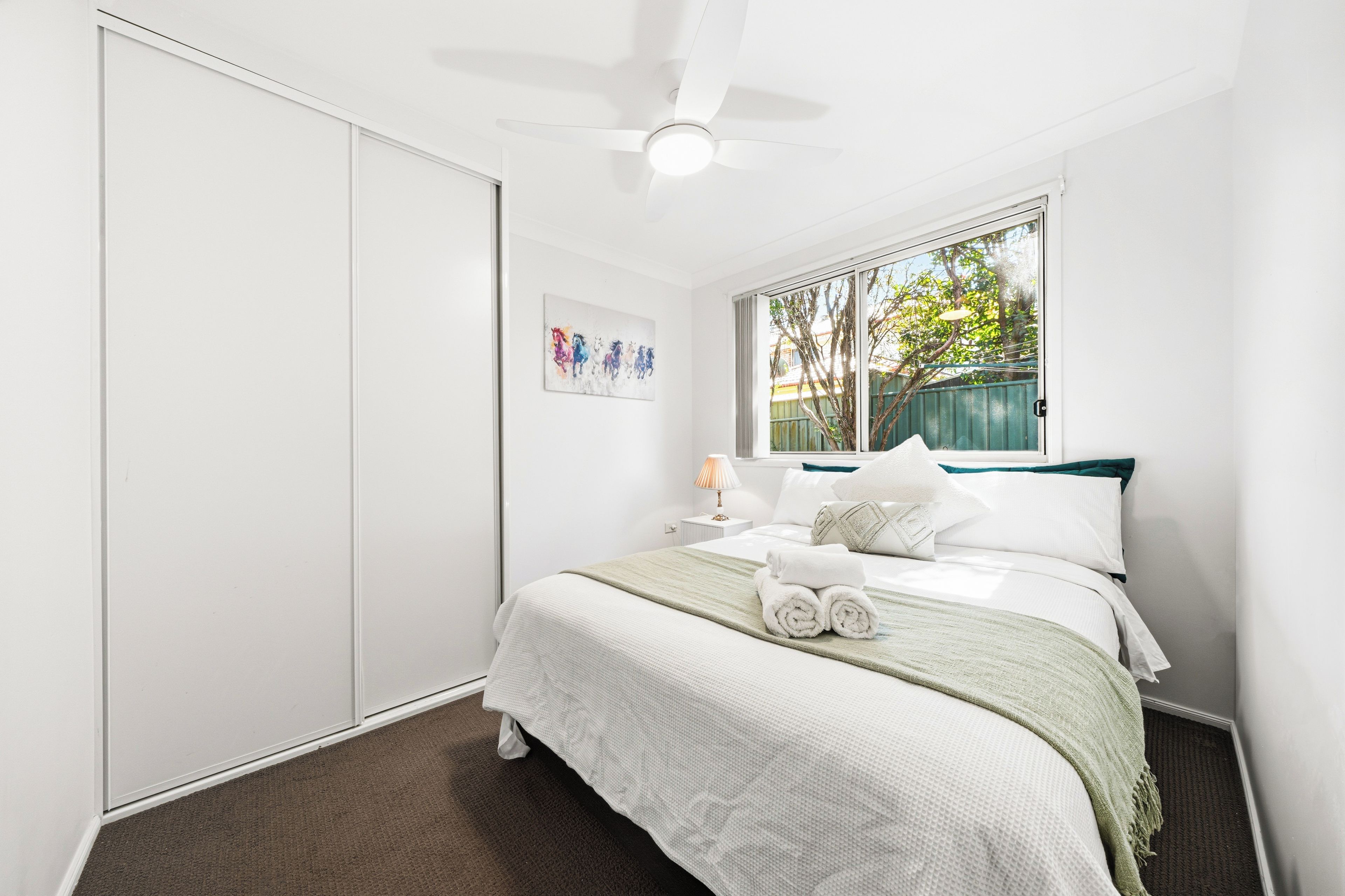 Una habitación de hotel con una cama, un ventilador de techo, una ventana con vistas al exterior y un cuadro en la pared.