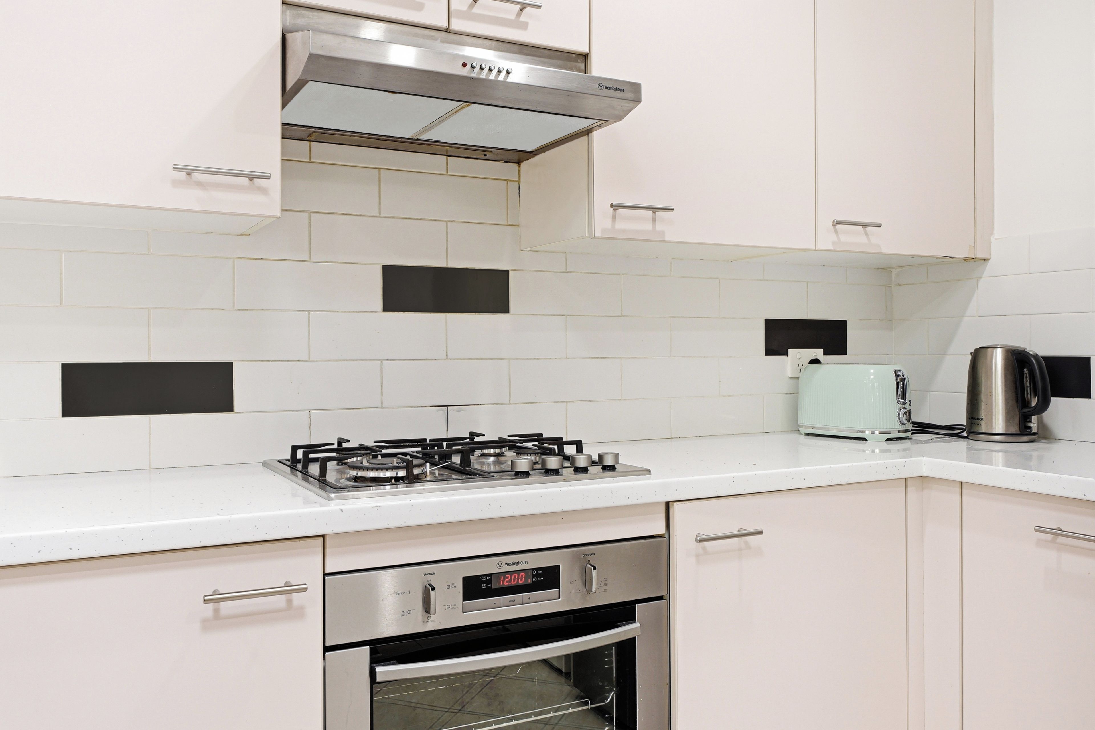 Una cucina moderna con mobili bianchi, una cappa aspirante in acciaio inossidabile, un piano cottura a gas, un forno integrato e un bollitore sul bancone.