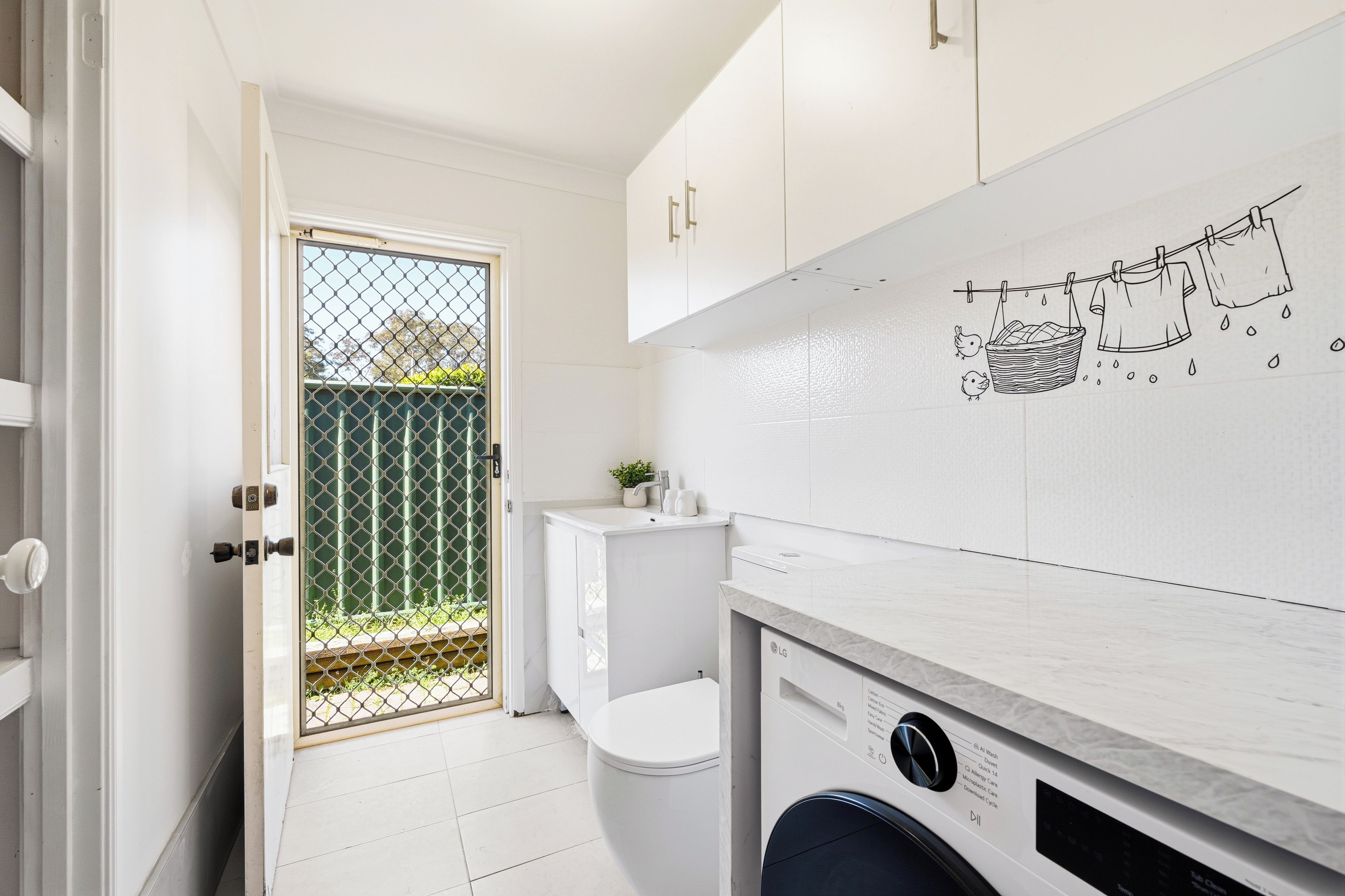 Una cocina moderna con armarios blancos, lavadora y salpicadero de azulejos.