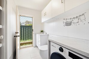 Een moderne keuken met witte kasten, een wasmachine en een betegelde spatwand.
