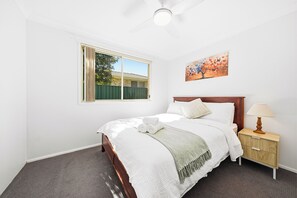 A hotel room with a bed, a nightstand, a lamp, a painting, and a window with a view of a building and greenery.