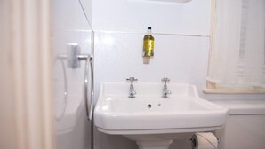 A bathroom with a white sink, two faucets, a toilet, and a shower. - Milton House Bed and Breakfast (Leyburn)