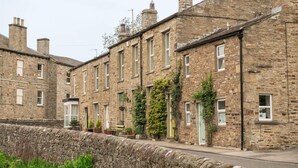 A row of stone buildings with uniform windows and doors, a stone wall in the foreground, and potted plants on the ground. - Milton House Bed and Breakfast (Leyburn)