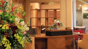 A reception desk with a wooden finish, a vase of flowers, and a seating area with chairs. - Beppu Fuga (Beppu)