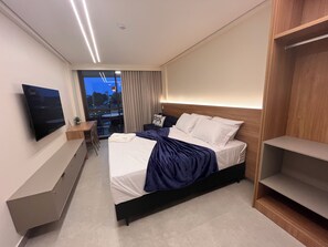 A modern hotel room with a bed, a TV, a desk, and a view of the city at dusk. - Sole e Mare Flat on Muro Alto beach. (N. Sra. do Ó)