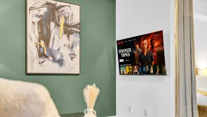 A room with a framed abstract painting, a wall-mounted Netflix display, and a small table with a decorative vase. - Harbourfront Retreat Near the Waterfront (Toronto)