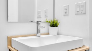 A bathroom with a white sink, chrome faucet, and a mirror above it. There is a potted plant on the sink's edge. - Harbourfront Retreat Near the Waterfront (Toronto)