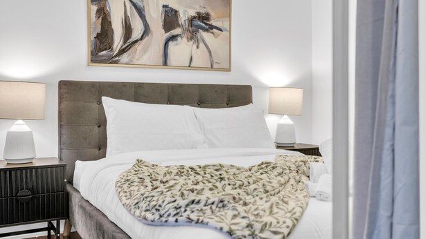 A hotel room with a large bed, two bedside lamps, a decorative painting, and a patterned throw blanket. - Harbourfront Retreat Near the Waterfront (Toronto)
