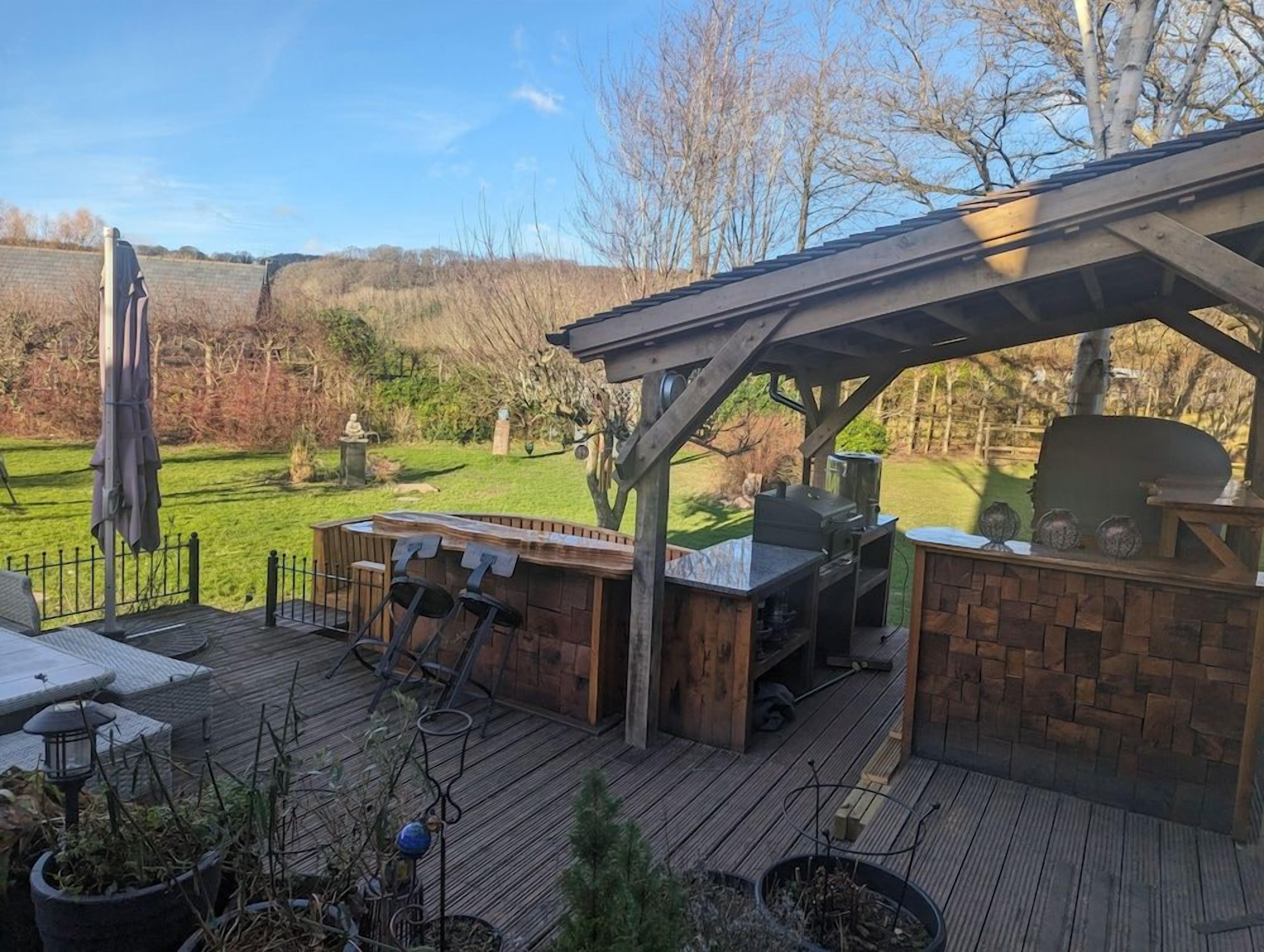 An outdoor patio with a grill and seating area, surrounded by a wooden deck and potted plants.