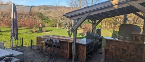 An outdoor patio with a grill and seating area, surrounded by a wooden deck and potted plants.