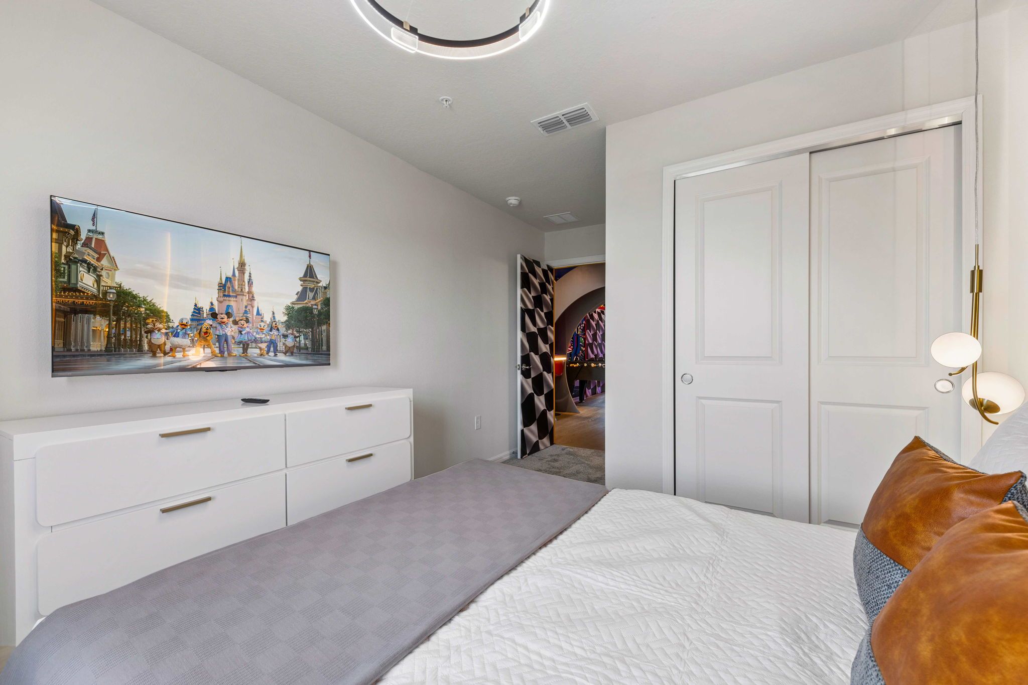 A bedroom with a bed, a dresser, a television on the wall, and a door leading to another room.