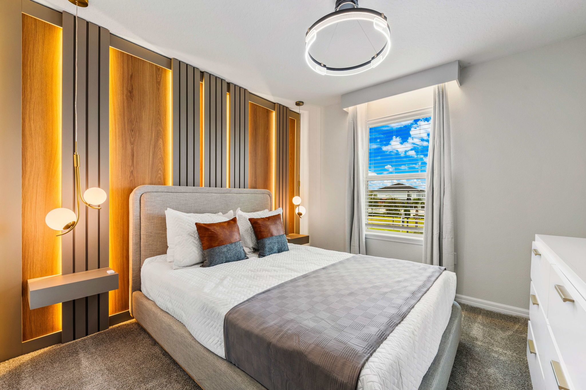 A modern bedroom with a bed, bedside lamps, and a view of the sky through the window.