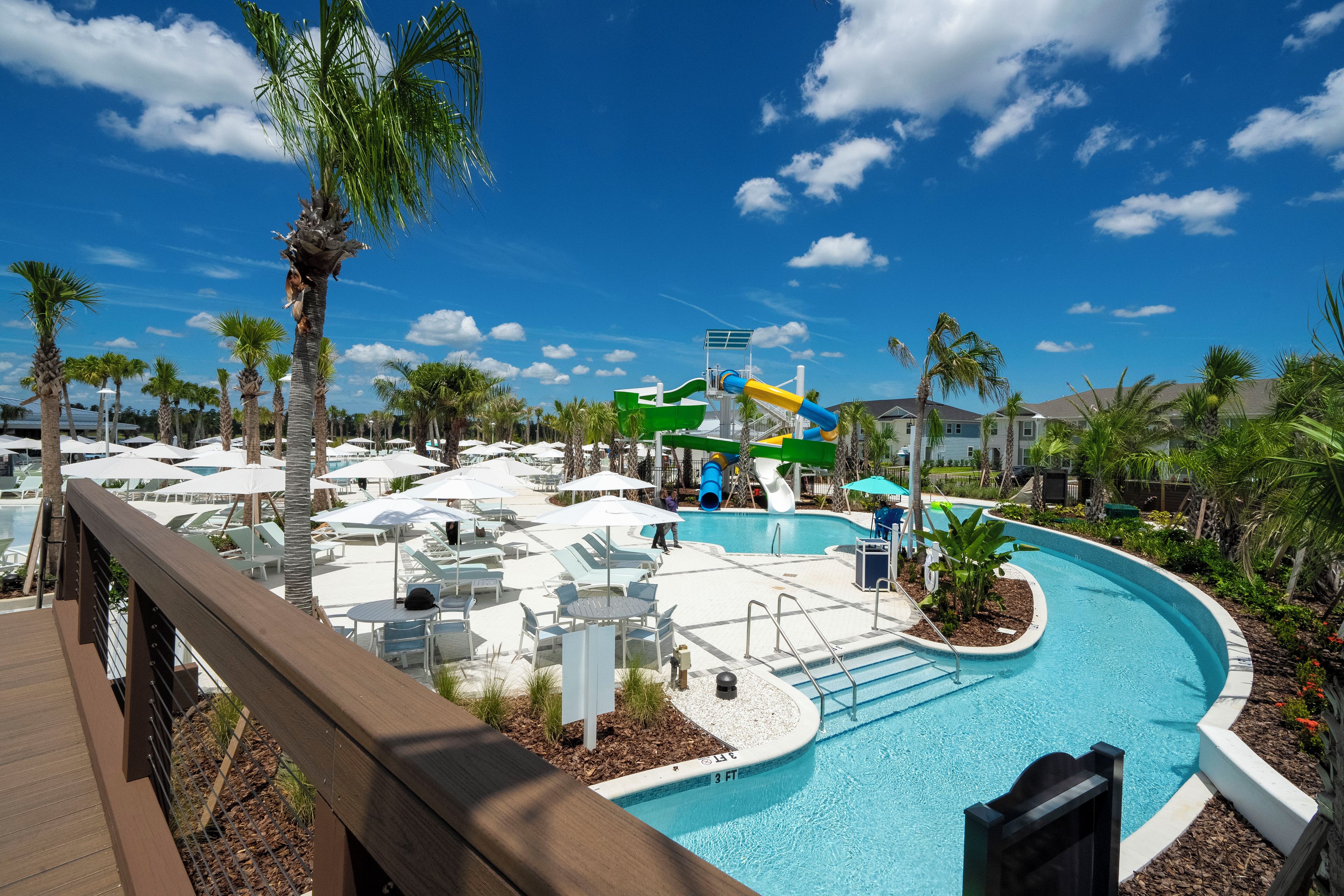 A pool area with lounge chairs and umbrellas, a water slide, and palm trees.