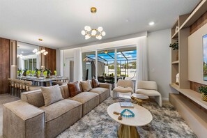 A modern living room with a sectional sofa, a coffee table, and a dining area with a table and chairs. - Brand New | Modern 5BR with Pool & Game Room 16212 (Clermont)