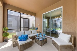 A sunlit patio with wicker furniture, a glass door leading outside, and a small potted plant. - Brand New | Family 6BR Pool Spa & Game Lounge 7875 (Kissimmee)