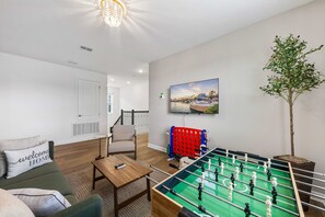Ein Wohnzimmer mit einem Fußballtisch, einer Couch, einem Couchtisch und einem an der Wand montierten Fernseher.