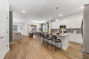 A modern kitchen with white cabinets, stainless steel appliances, and a central island with bar stools. - Brand New | Family 6BR Pool Spa & Game Lounge 7875 (Kissimmee)