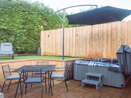 Un patio exterior con terraza de madera, un jacuzzi y una mesa con sillas.