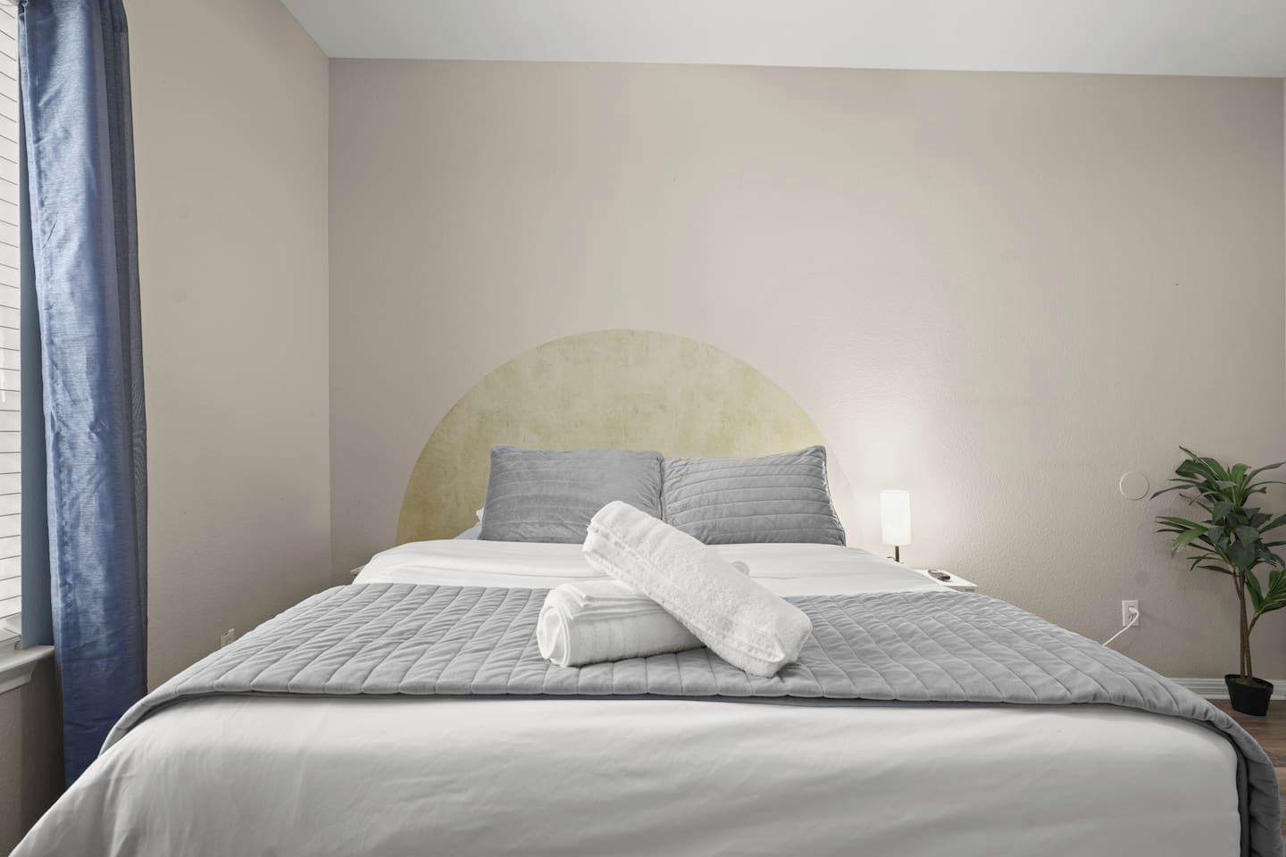 A neatly made bed with a headboard, a bedside lamp, and a potted plant.