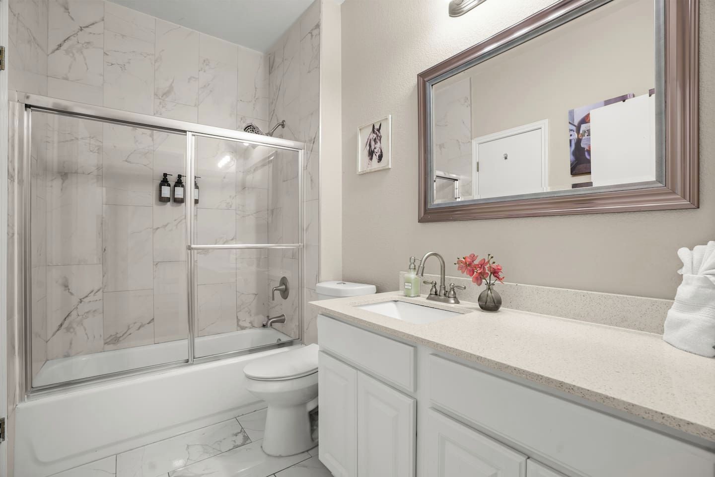 A bathroom with a glass-enclosed shower, a toilet, a sink with a mirror, and a vase with flowers.