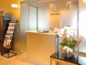 Un área de recepción con mostrador, un reloj, un letrero que dice 'Live Max' y un arreglo floral.