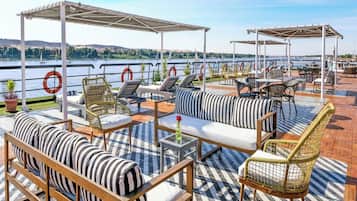 Une terrasse avec des sièges extérieurs, comprenant des canapés et des fauteuils, donnant sur une étendue d’eau où se trouvent des bateaux.