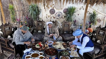 A group of people seated at a table with various dishes, in a room with patterned walls and traditional furniture.