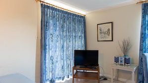 Una habitación con una televisión sobre un soporte de madera, un cuadro en la pared y un escritorio con un florero y altavoces.
