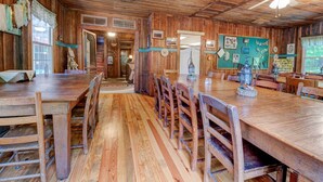 Un comedor rústico de madera con una mesa larga y sillas, un ventilador de techo y una pared verde con varias decoraciones.