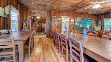 A rustic wooden dining area with a long table and chairs, a ceiling fan, and a green wall with various decorations.