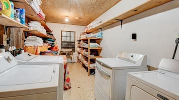 Une buanderie équipée de deux machines à laver, d’étagères où sont pliés les vêtements et de produits de lessive.