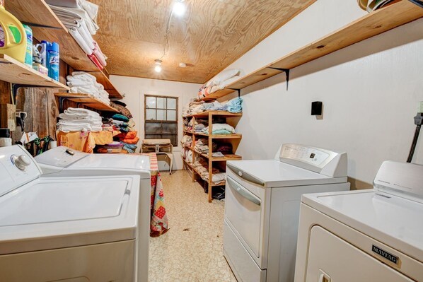 A laundry room with two washing machines, shelves with folded clothes, and laundry supplies.
