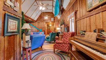 A cozy room with a wooden interior, a blue sofa, a red patterned armchair, a wooden piano, and a ceiling fan.