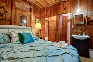 A wooden-paneled room with a bed, a nightstand, a lamp, a mirror, and a sink.