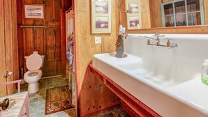 Un baño de madera con una bañera blanca, un inodoro y fotografías enmarcadas en la pared.