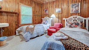 Habitación con paneles de madera, dos camas, una silla roja, una lámpara y una ventana con persianas.