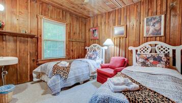 A wooden-paneled room with two beds, a red chair, a lamp, and a window with blinds.