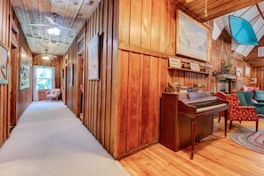 A wooden interior with a piano, chairs, and a hallway leading to a window.