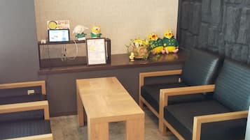 A reception area with a wooden desk, two chairs, a small table, and decorative items including a laptop, framed picture, and figurines.