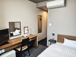 Quarto de hotel com cama, escrivaninha com telefone, espelho e ar condicionado.